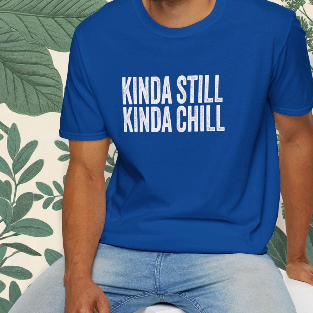 Man wearing a blue t-shirt with 'KINDA STILL KINDA CHILL' text, sitting on a white stool with a green leafy background.