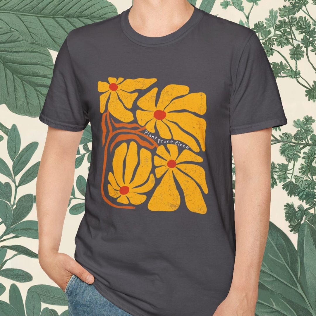 Person wearing a dark gray t-shirt with a yellow floral design, standing against a leafy background.