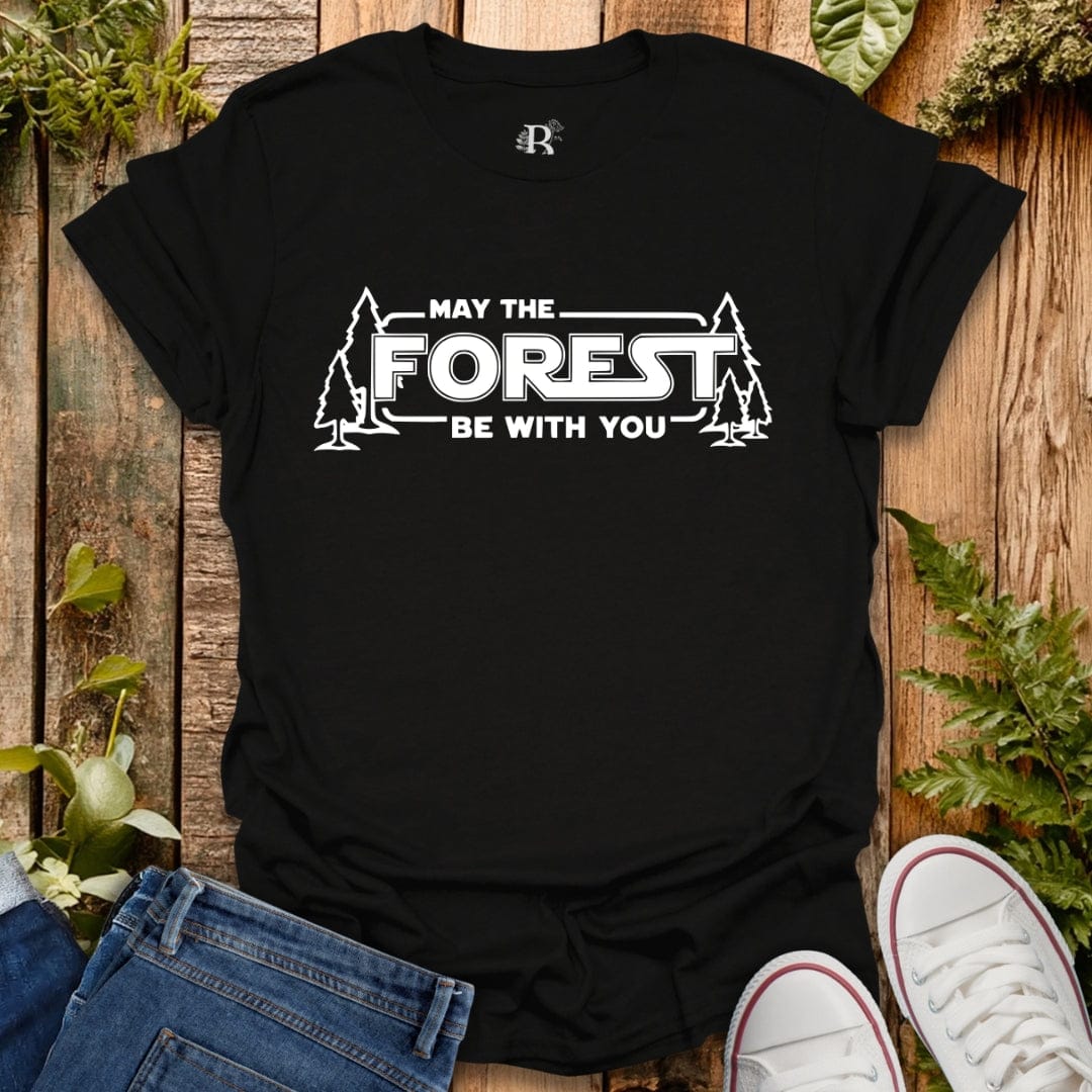 Black t-shirt with 'May the Forest Be With You' design on a wooden background with plants.