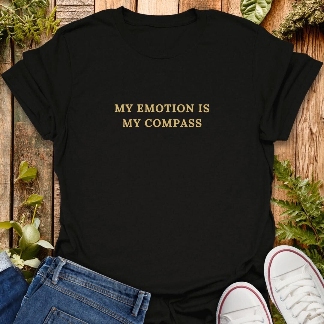 Black t-shirt with 'My emotion is my compass' text, paired with jeans and white sneakers on a wooden background.