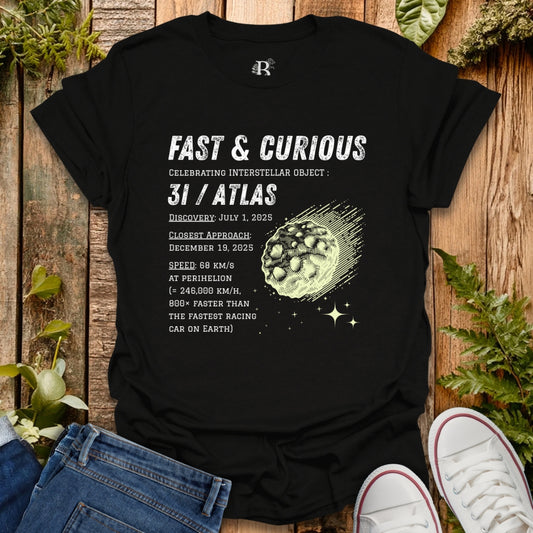 Black t-shirt with 3I/Atlas space-themed design on a wooden surface with plants.