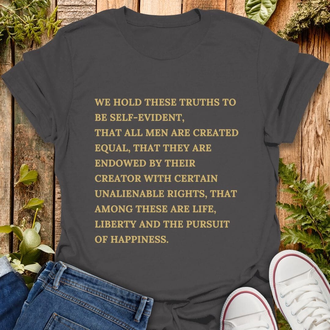 Gray t-shirt with declaration of independence text on a wooden background with plants, jeans and sneakers.