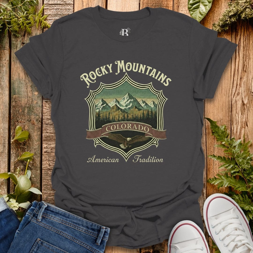 Gray t-shirt with 'Rocky Mountains Colorado' design on a wooden surface with jeans and sneakers.
