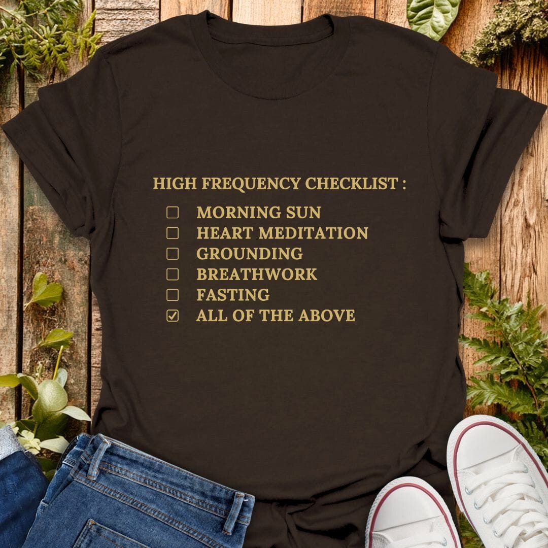 Brown t-shirt with 'High Frequency Checklist' text on a wooden surface with plants, jeans and sneakers.