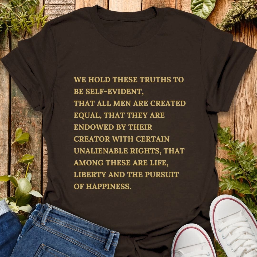 Brown t-shirt with declaration of independence text on a wooden background with plants, jeans and sneakers.