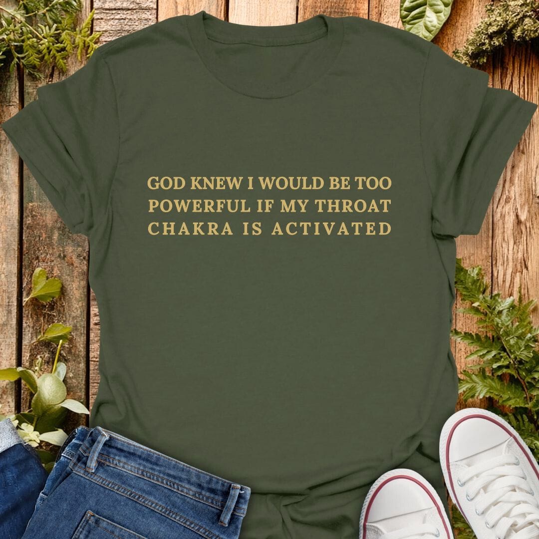Green t-shirt with "God knew I would be too powerful if my throat chakra is activated" text on a wooden background with plants, jeans, and sneakers.