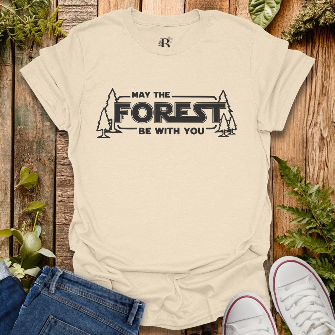 Beige t-shirt with 'May the Forest Be With You' text on a wooden background with plants.