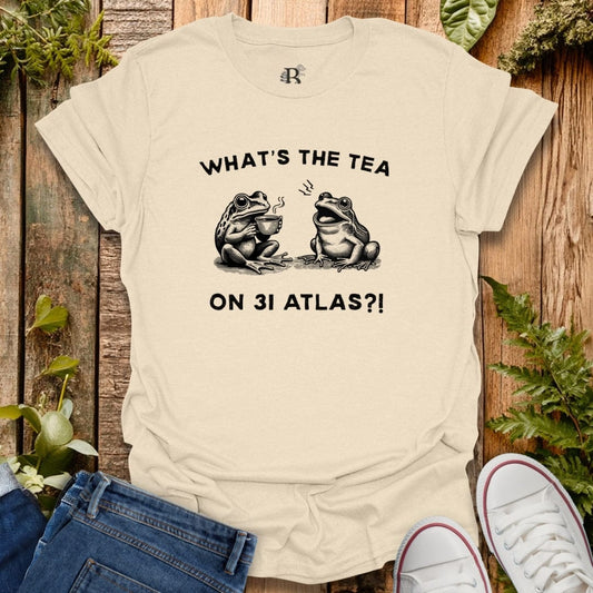 Natural t-shirt with frogs design qnd text 'What's the tea on 3I Atlas?!'.