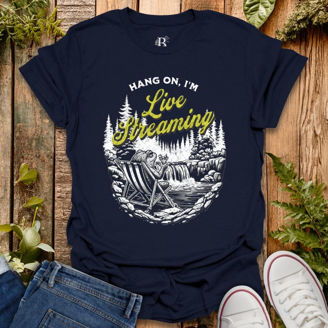 Navy blue t-shirt with graphic design and text 'Hang on, I'm Live Streaming' on a wooden background.