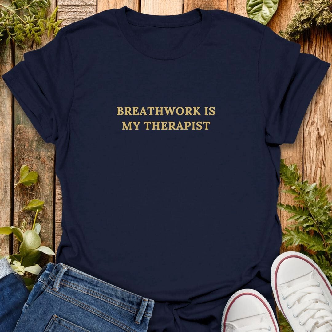 Navy blue t-shirt with 'Breathwork is my therapist' text, paired with jeans and white sneakers on a wooden background.