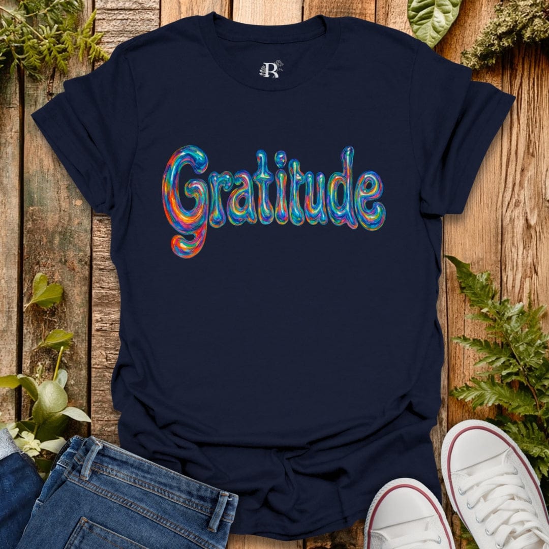 Navy blue t-shirt with 'Gratitude' in colorful letters on a wooden surface with plants.