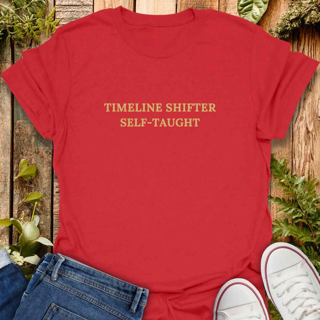 Red t-shirt with 'TIMELINE SHIFTER SELF-TAUGHT' text, paired with jeans and white sneakers on a wooden surface.