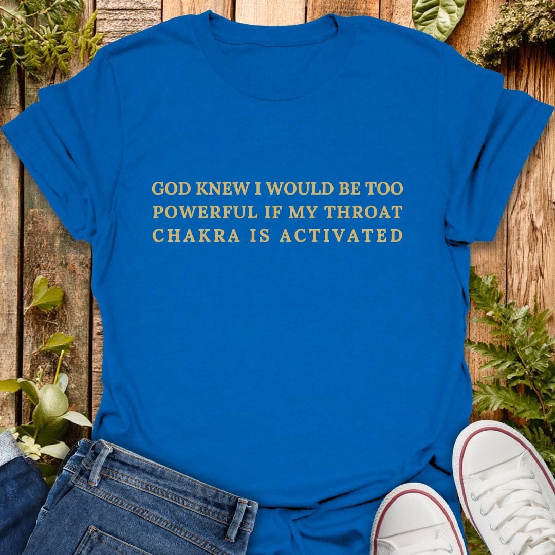 Blue t-shirt with "God knew I would be too powerful if my throat chakra is activated" text on a wooden background with plants, jeans, and sneakers.