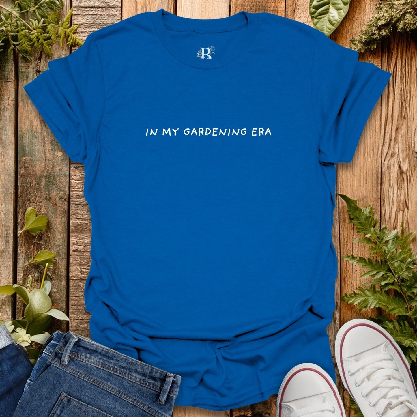 Blue t-shirt with 'IN MY GARDENING ERA' text on a wooden background with plants.