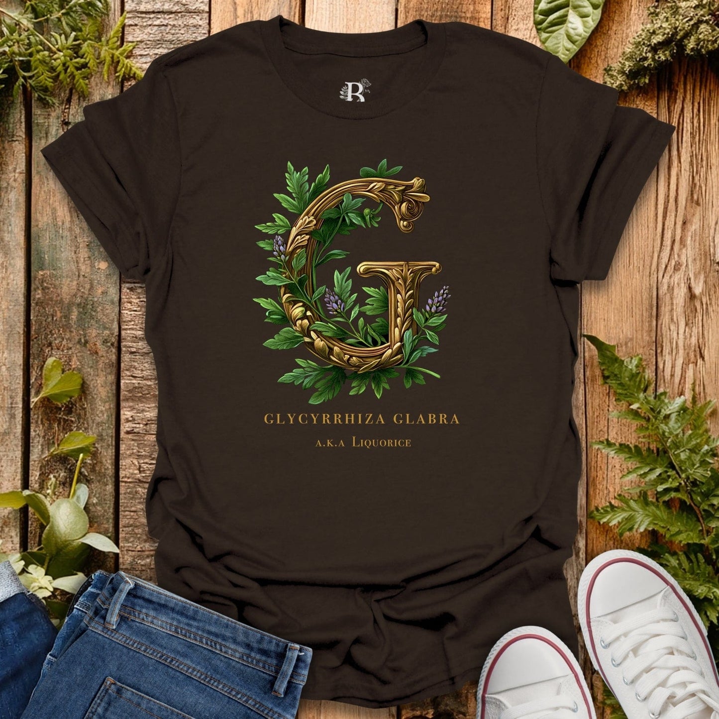 Black t-shirt with gold letter 'G' and green leaves on a wooden surface with plants.