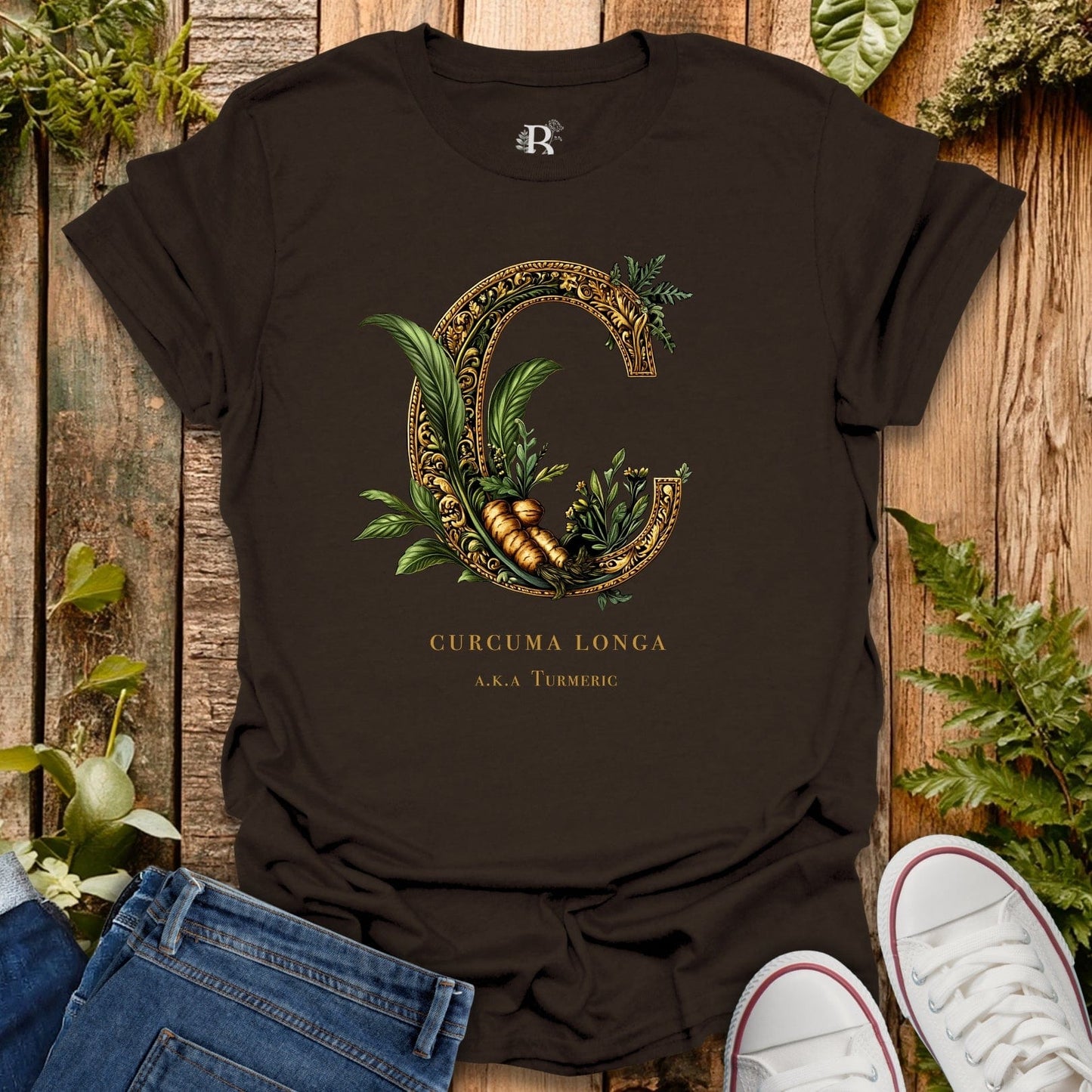 Black t-shirt with decorative letter 'C' design and text on a wooden surface with plants.