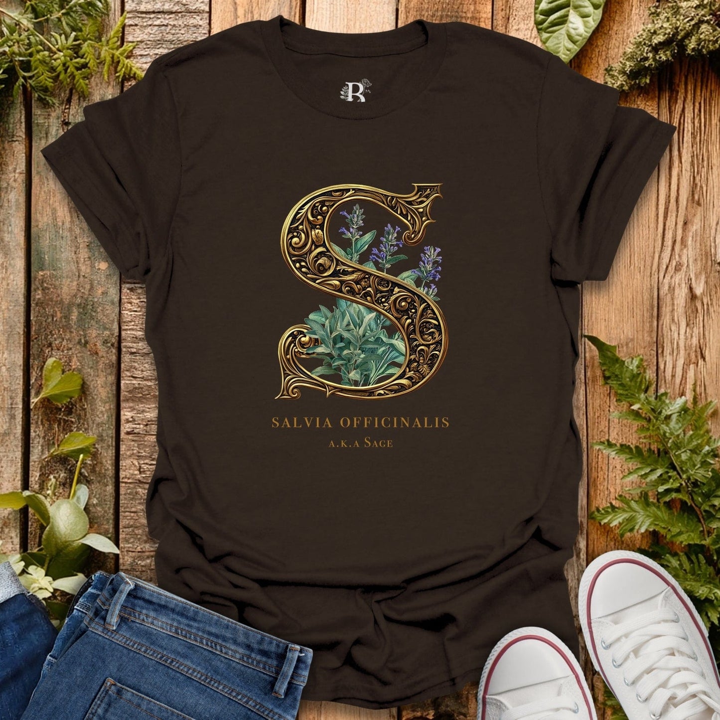 Black t-shirt with decorative letter 'S' and plant design on a wooden surface with plants around.