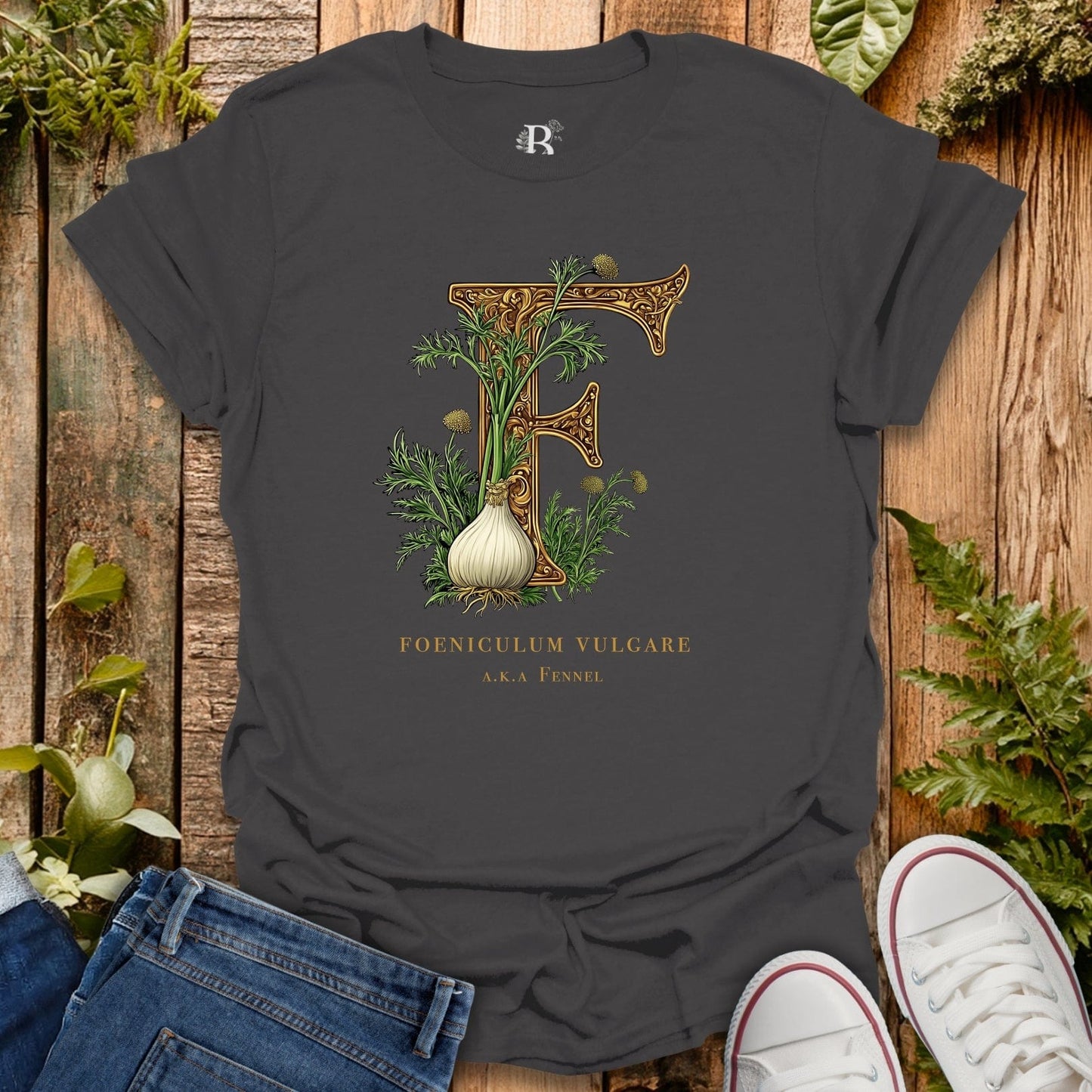 Dark gray t-shirt with fennel plant design on a wooden surface with plants around