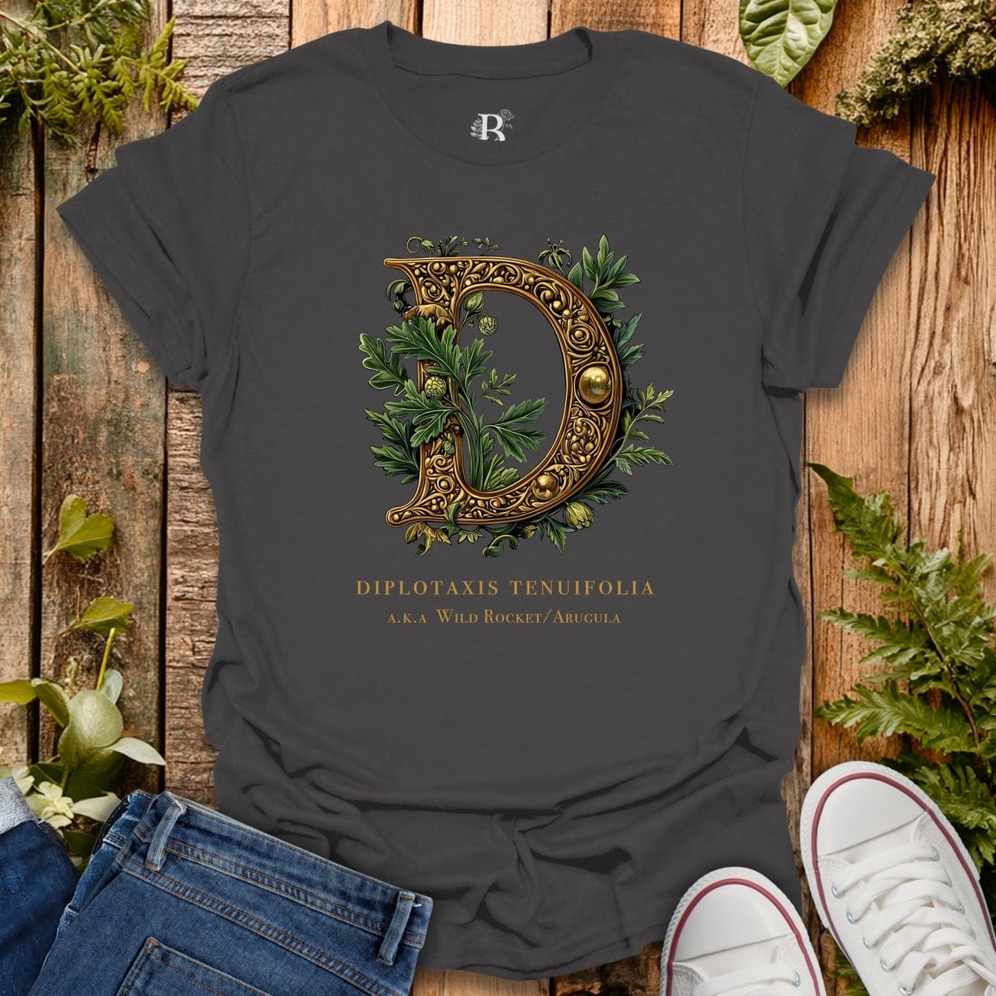Dark gray t-shirt with decorative letter 'D' design on a wooden surface with plants.