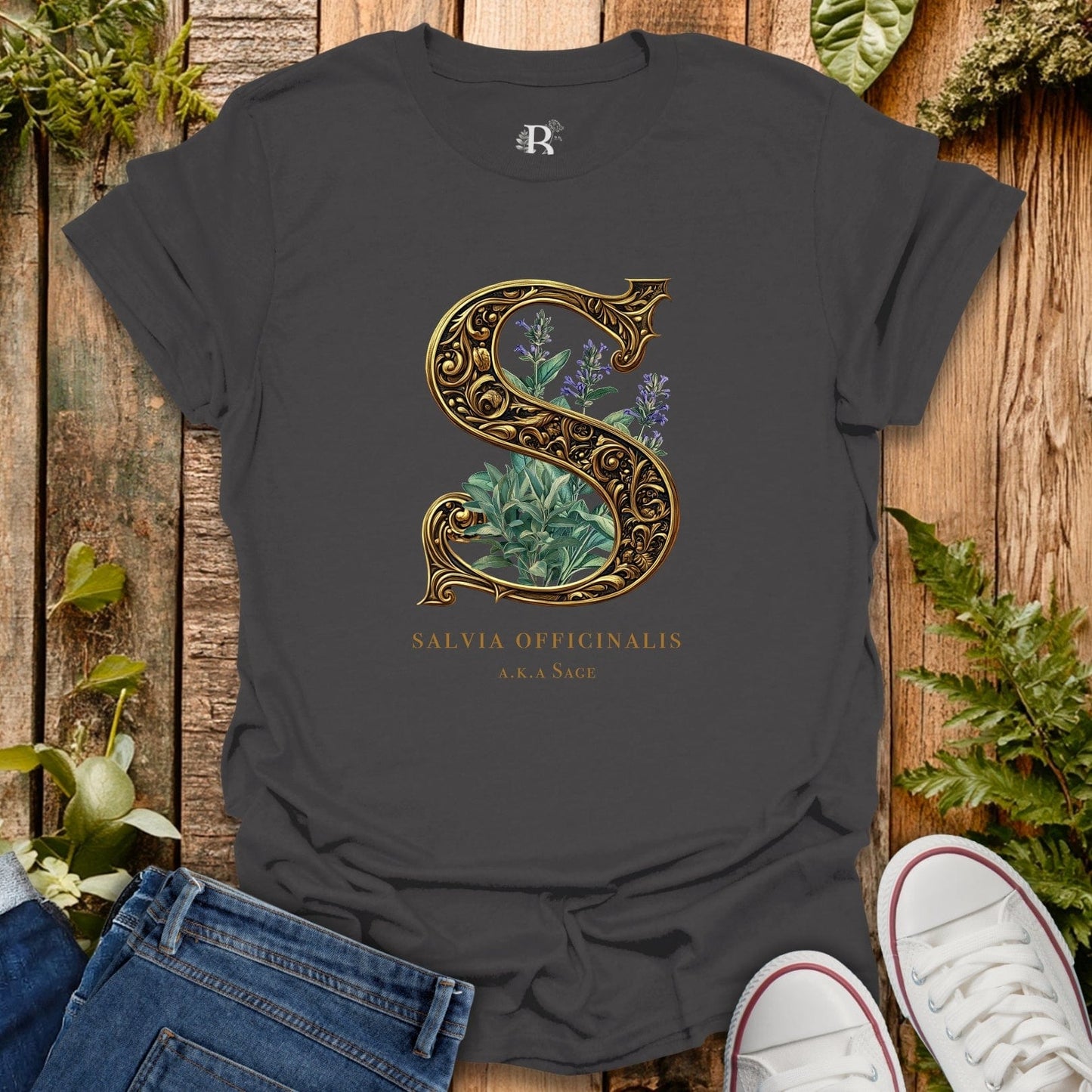 Dark gray t-shirt with decorative letter 'S' design featuring plants on a wooden surface with plants around.