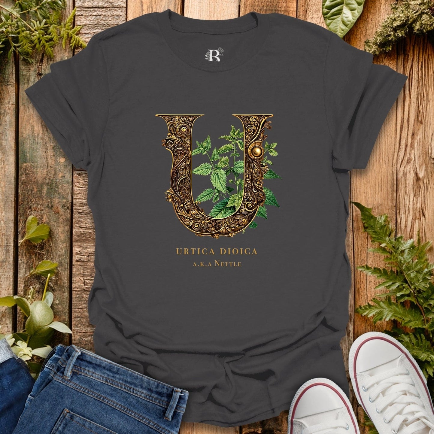 Dark gray t-shirt with decorative letter 'U' design featuring leaves on a wooden surface with plants.