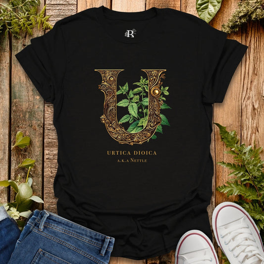 Black t-shirt with decorative letter 'U' design featuring leaves on a wooden surface with plants.