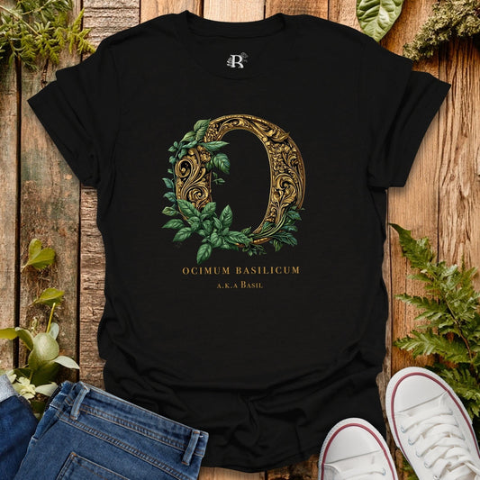 Black t-shirt with decorative letter 'O' design featuring leaves on a wooden surface with plants.