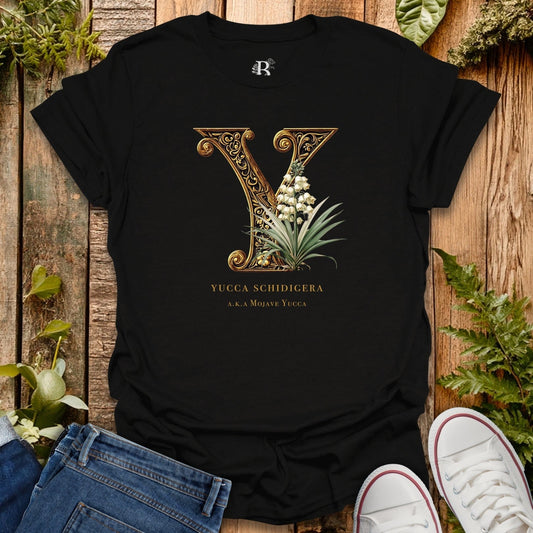 Black t-shirt with decorative letter 'Y' design on a wooden surface with plants.
