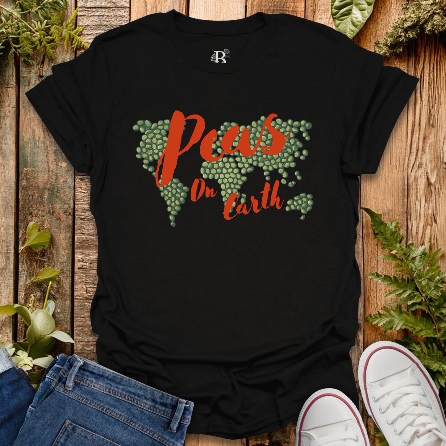 Black t-shirt with 'Peas on Earth' design on a wooden surface with plants.