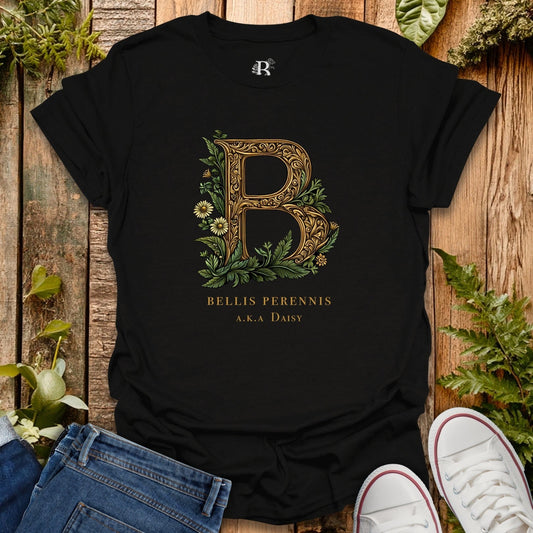 Black t-shirt with floral letter 'B' design on a wooden surface with plants.
