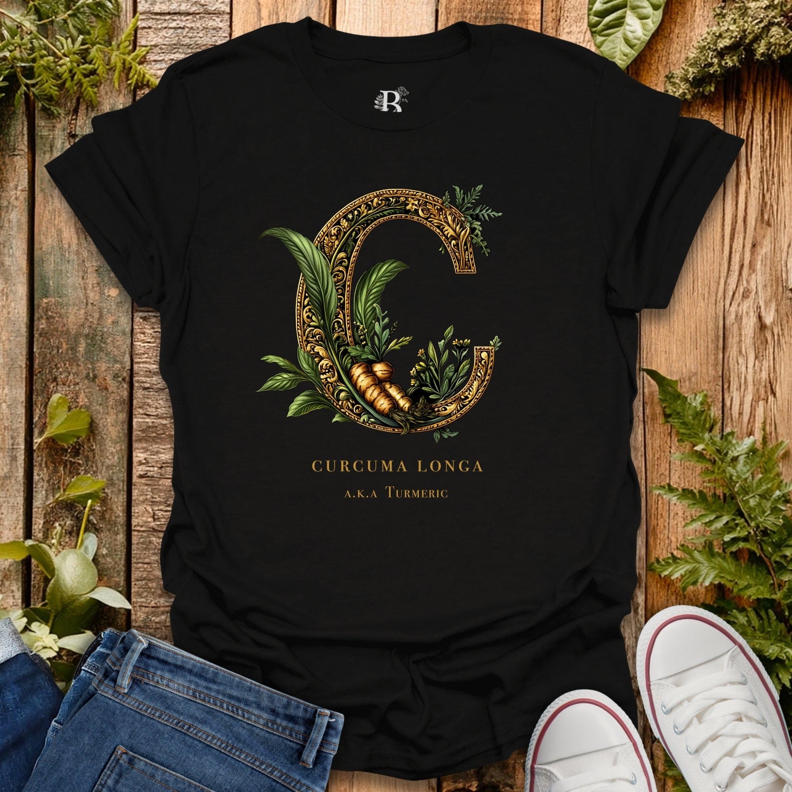 Black t-shirt with gold and green design on a wooden surface with plants.
