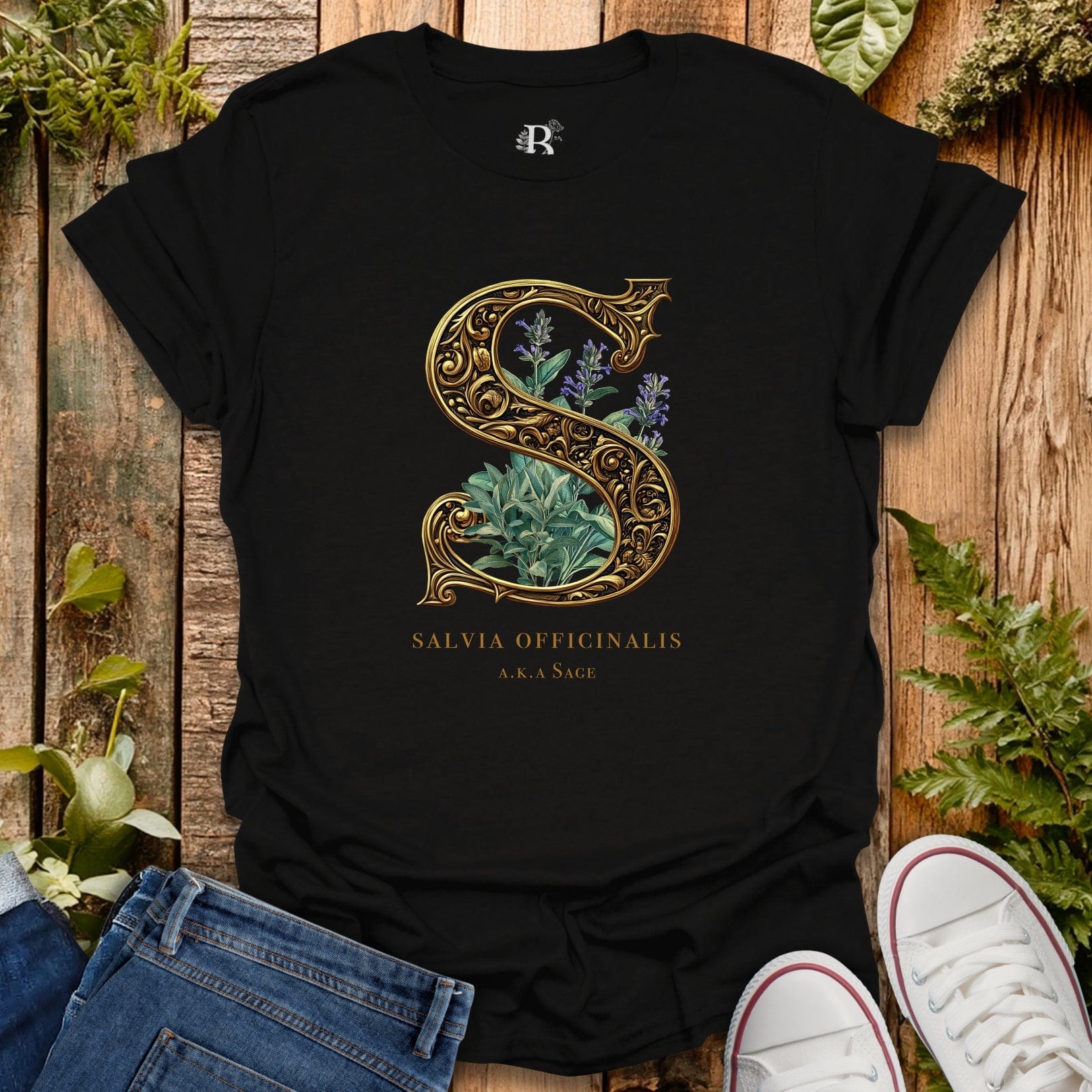 Black t-shirt with decorative letter 'S' design featuring plants on a wooden surface with plants around.