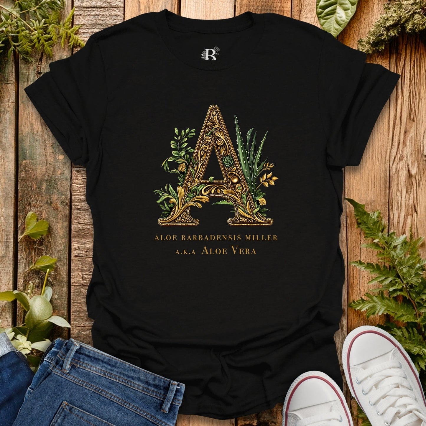 Black t-shirt with a gold letter 'A' design on a wooden surface with plants.