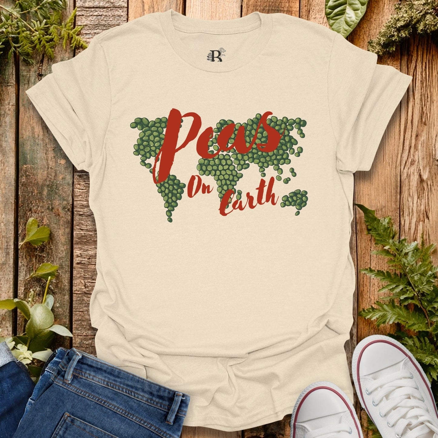 Beige t-shirt with 'Pews On Earth' design on a wooden background with plants.