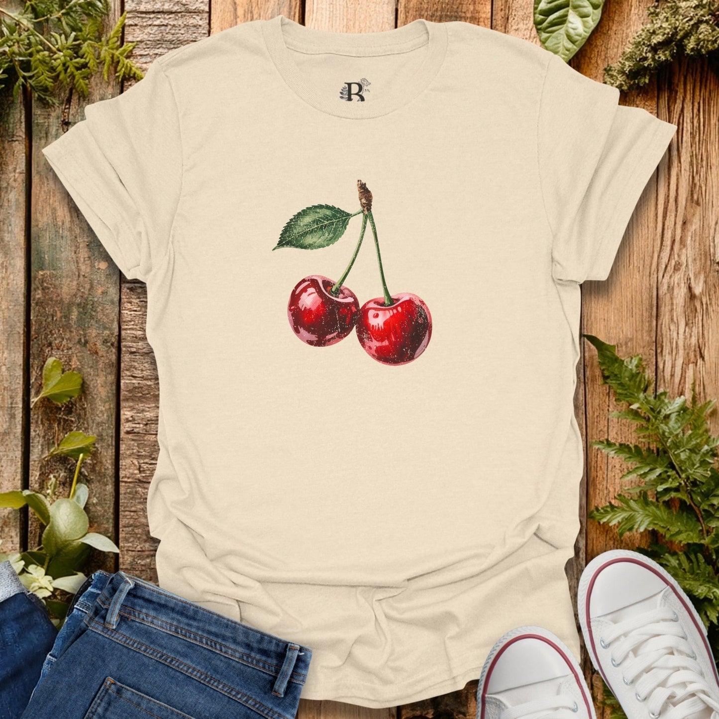 Beige t-shirt with cherry design on a wooden surface with plants.