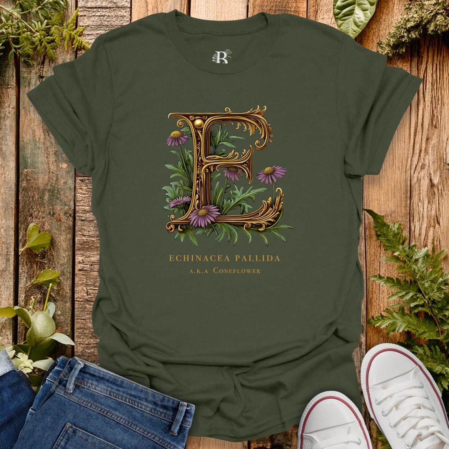 Green t-shirt with decorative letter 'E' and floral design on a wooden surface with plants.