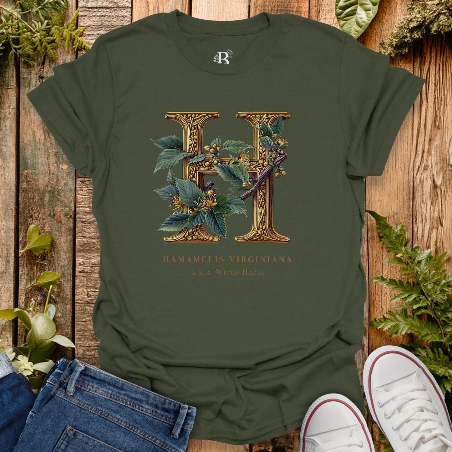 Green t-shirt with floral letter 'H' design on a wooden surface with plants.