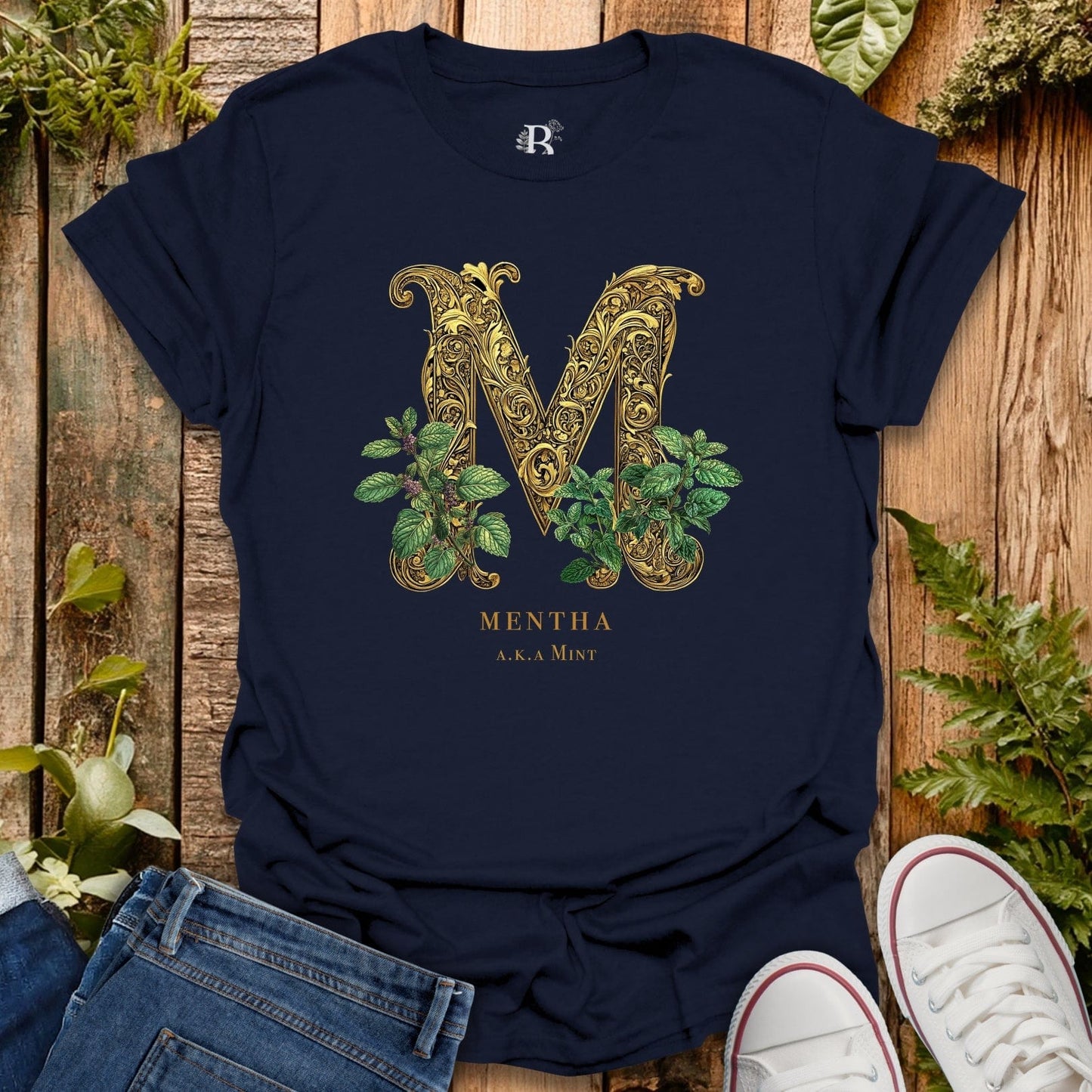 Navy blue t-shirt with gold letter 'M' design on a wooden surface with plants.