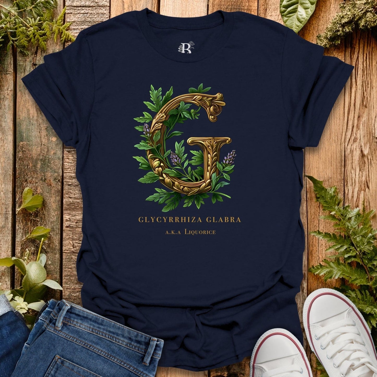 Navy blue t-shirt with gold letter 'G' and green leaves on a wooden surface with plants.