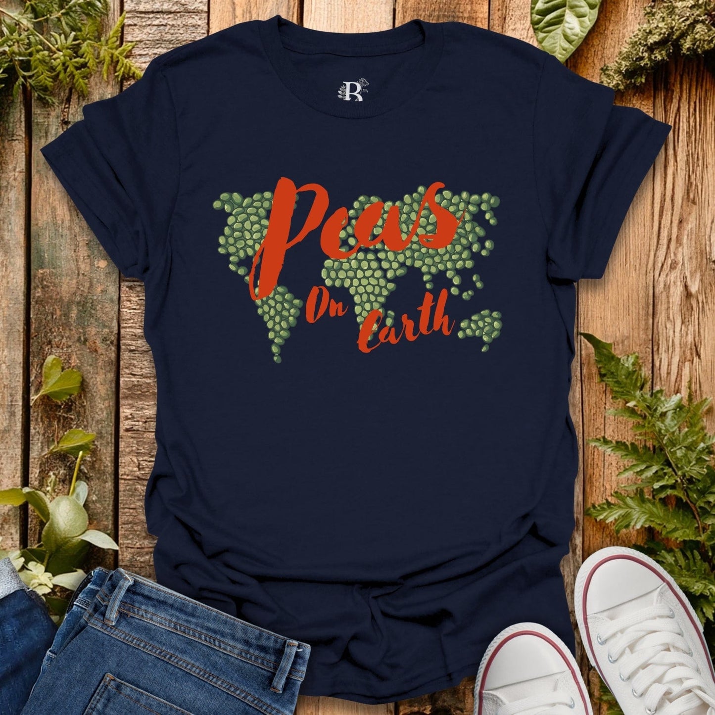 Navy blue t-shirt with 'Peas on Earth' graphic design on a wooden surface with plants.