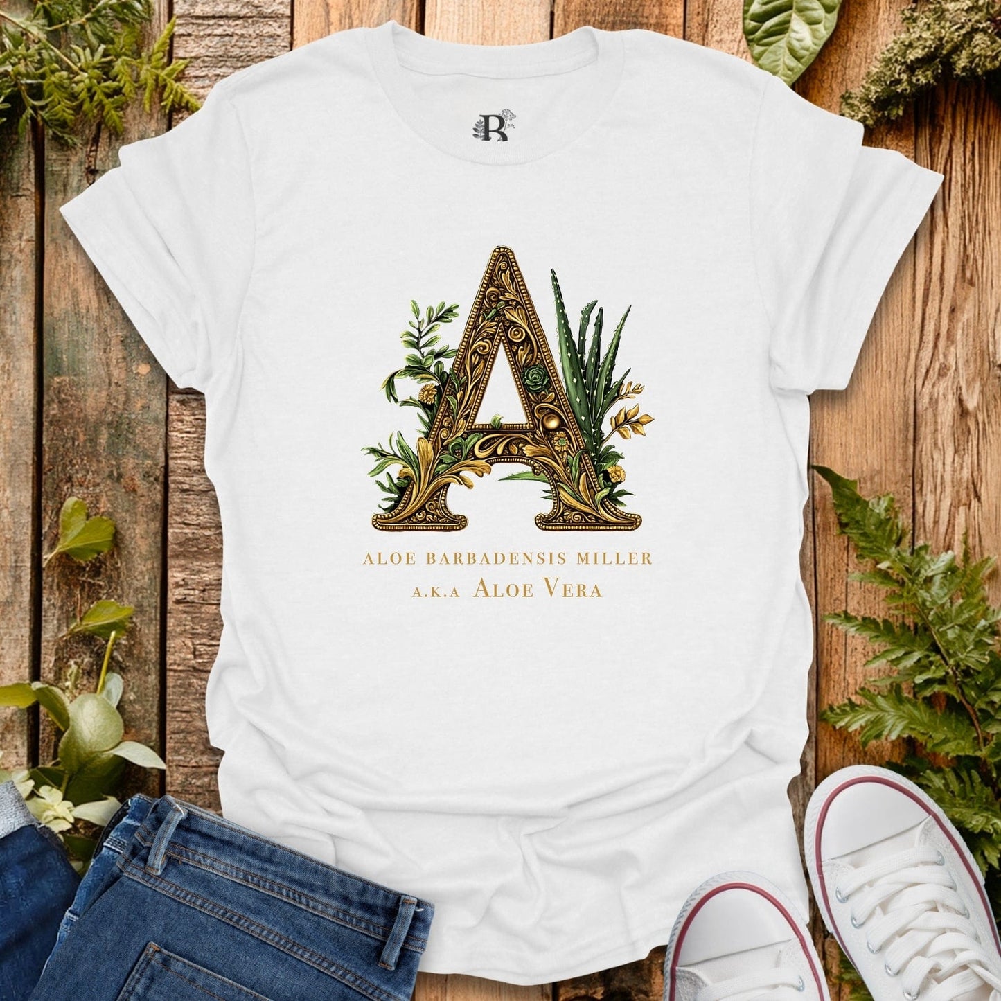 White t-shirt with decorative letter 'A' design on a wooden surface with plants.