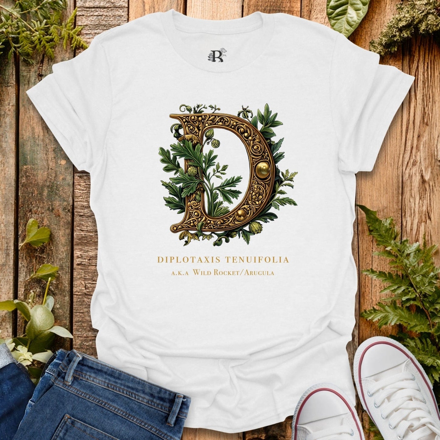White t-shirt with decorative letter 'D' design on a wooden surface with plants.