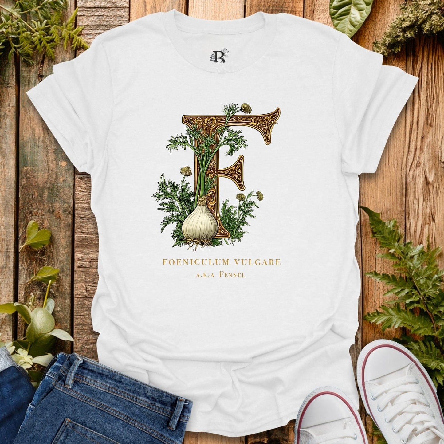White t-shirt with fennel illustration and text on a wooden surface with plants.