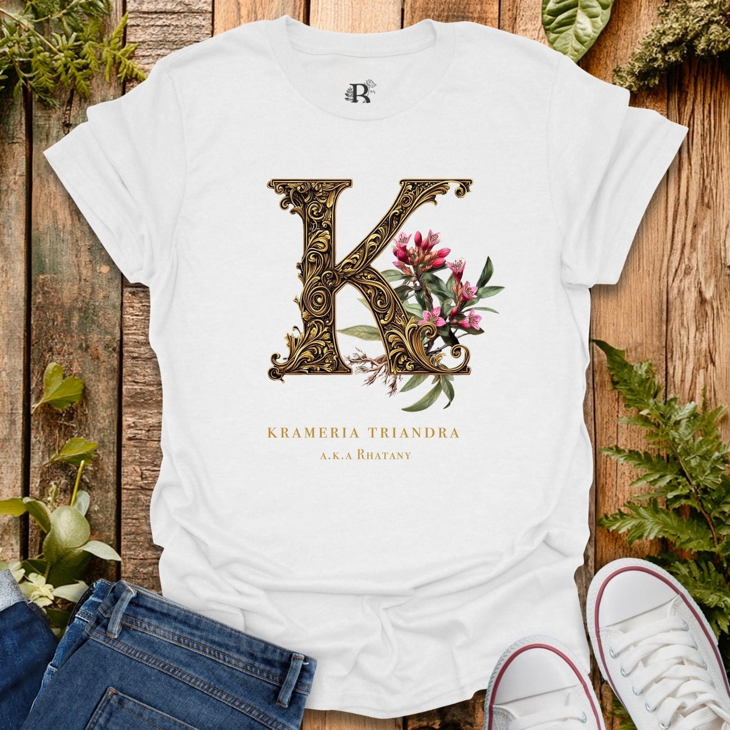 White t-shirt with decorative letter 'K' design on a wooden surface with plants.