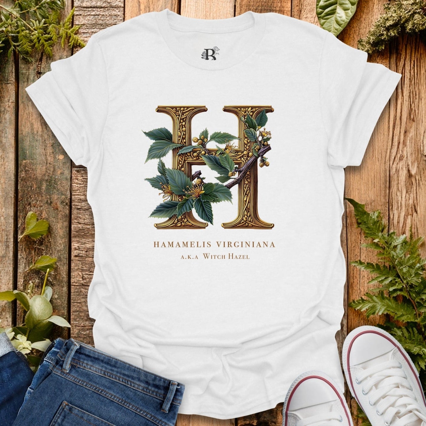 White t-shirt with decorative letter 'H' design on a wooden surface with plants.