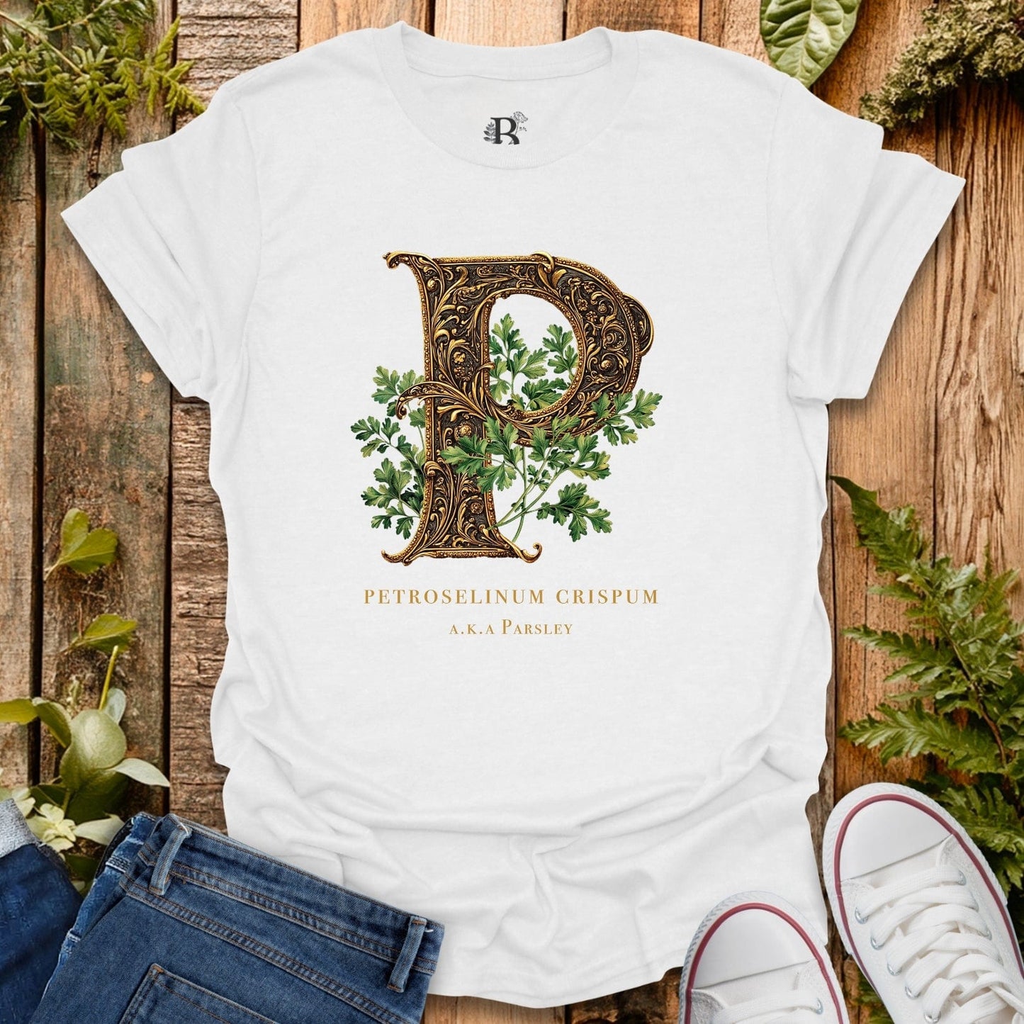 White t-shirt with decorative letter 'P' and plant design on a wooden surface with plants around.
