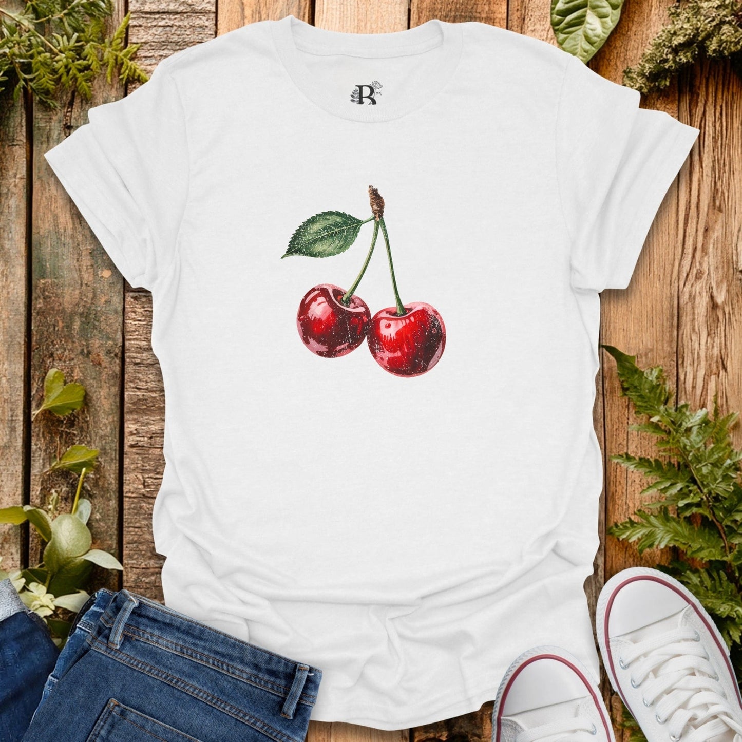 White t-shirt with cherry design on a wooden surface with plants