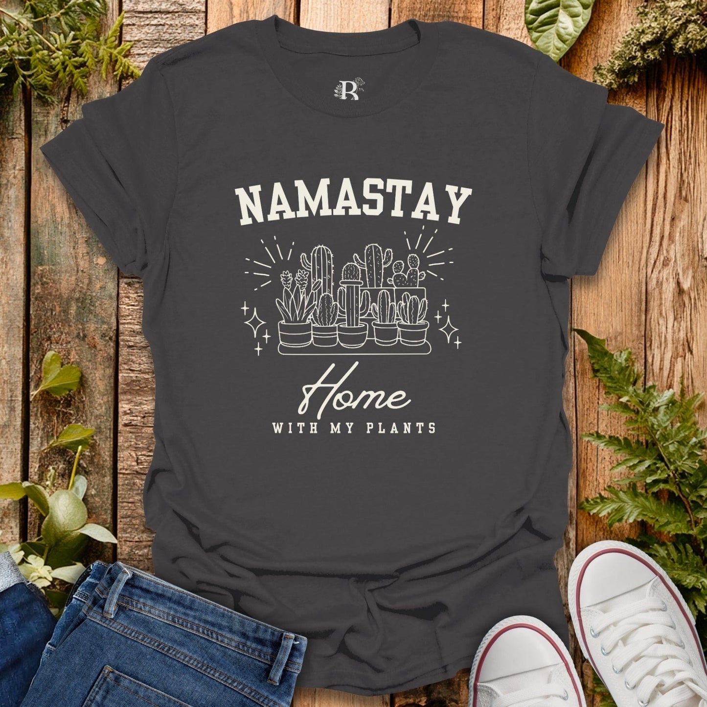 Black t-shirt with 'Namastay Home with My Plants' design on a wooden surface with plants.