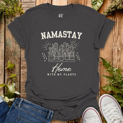 Black t-shirt with 'Namastay Home with My Plants' design on a wooden surface with plants.