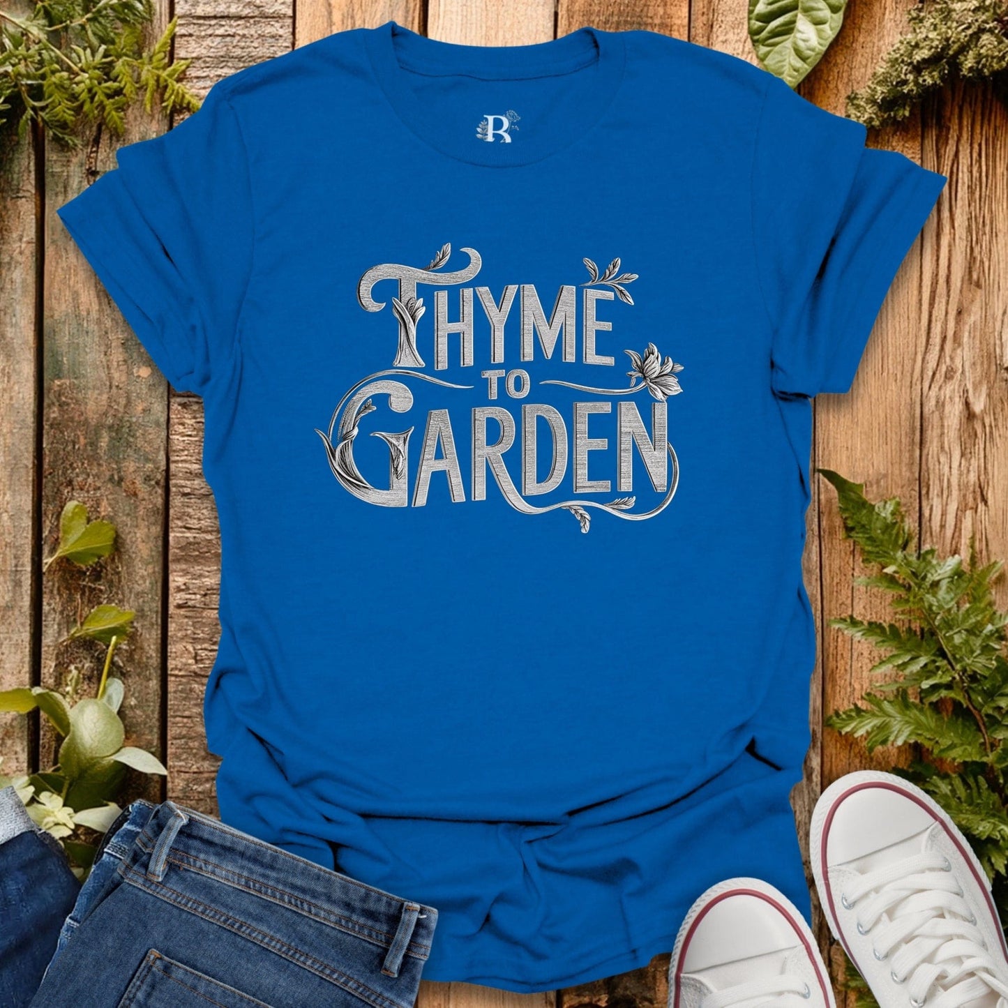 Blue t-shirt with 'Thyme to Garden' text on a wooden background with plants.